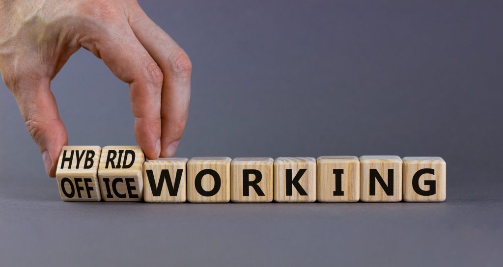 Hybrid or office working symbol. Businessman turns cubes and changes words 'office working' to 'hybrid working'. Beautiful grey background. Business, hybrid or office working concept, copy space.